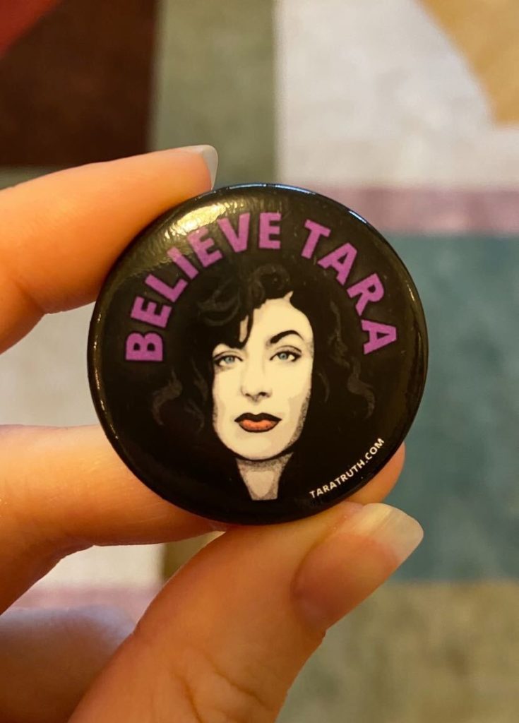 Believe Tara logo on a button, held up for size (about the size of a quarter). The logo is a picture of Tara's face, with Believe Tara above her.